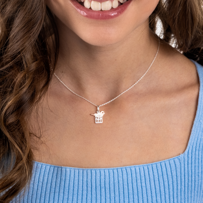 Teen wearing a rose gold bird in a sterling silver cage necklace. 